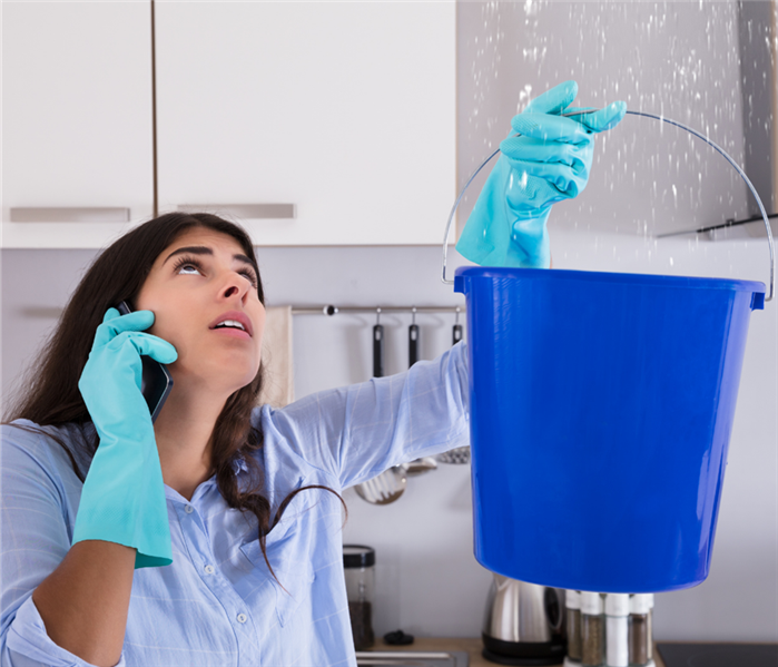A woman is holding a bucket under water coming from the ceiling.