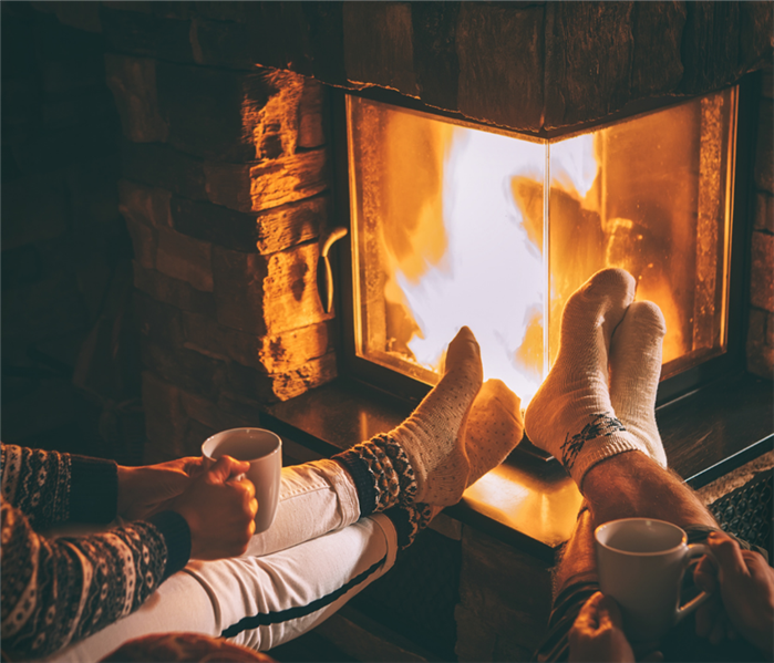 Man and woman wearing socks and holding mugs with feet up on the edge of indoor fireplace 